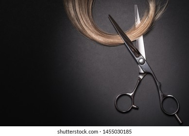 Scissors and piece of blond hair. Professional barber hair cutting shears on black background. Hairdresser salon equipment concept, premium hairdressing set. Accessories for haircut with copy space